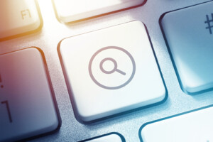 Magnifying glass icon graphic as search button on white keyboard.
