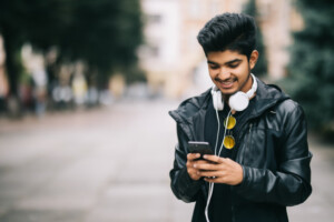 Happy indian man walking using smart phone listen music with headphones 231208 2769